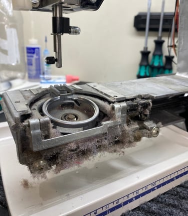The bobbin area of a sewing machine with covers removed, revealing a large build-up of dust and lint