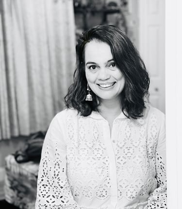 Smiling woman with wavy hair wearing a white eyelet lace blouse and jhumka earrings.