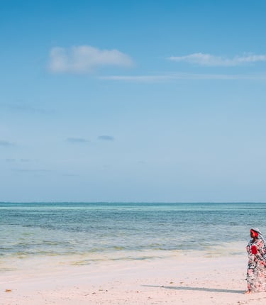 a woman in a red dress walking on a beach of Zanzibar