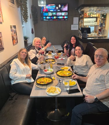 A group of smiling customers enjoying paella and drinks together in a cozy Spanish restaurant.