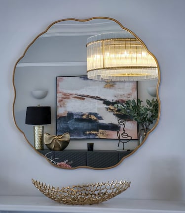 Gold-framed mirror reflecting modern decor with chandelier, abstract art, and stylish accents