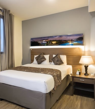 A modern interior space featuring a dining area with a table and chairs near the center. Adjacent are two bedrooms, each with furniture like beds and wardrobes, and a bathroom with a tiled shower. The space is well-lit with large windows and has neutral-toned floors and walls.