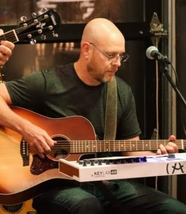 William Finn of Finn's Echo playing in front of a live audience at an open-mic night event.