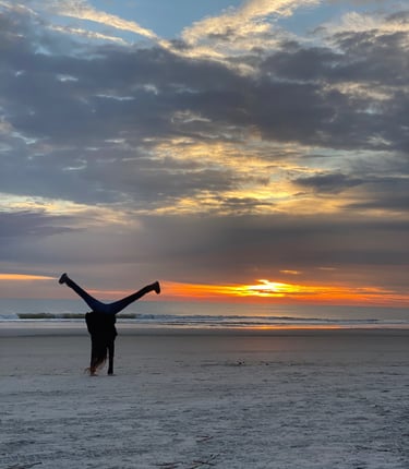 A woman doing a cartwheel on the beach silhouetted by the sunrise