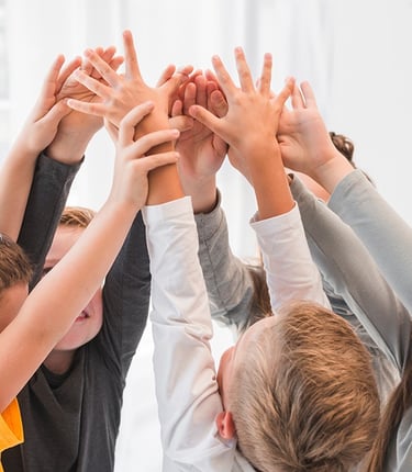 Kinder in der Spielgruppe der Zukunft heben gemeinsam die Hände – Förderung von Teamgeist und sozial