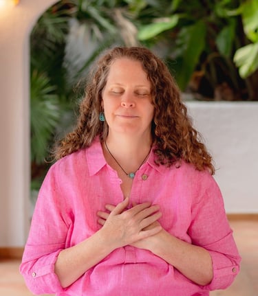 Sheila Doerfler in magenta blouse sitting cross legged with hands on heart center eyes closed