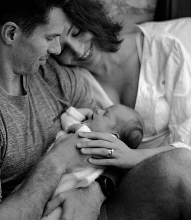 a newborn in her mom & dads arms, looking down at her in a lifestyle newborn shoot