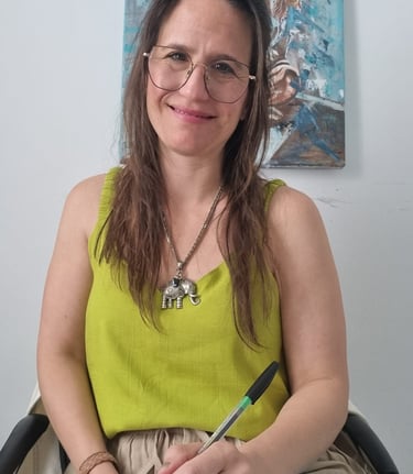 A smiling professional woman with glasses and an elephant necklace holding a pen and notepad.