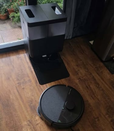 Robot vacuum positioned near its self-emptying dock on a hardwood floor by a window