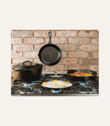 pciture of black Lodge 12 inch cast iron skillet on the back brick wall of a kitchen, behind a stove