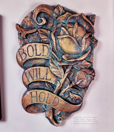 A plaque in the style of traditional tattoo art. A rose with a banner that says Bold Will Hold. 
