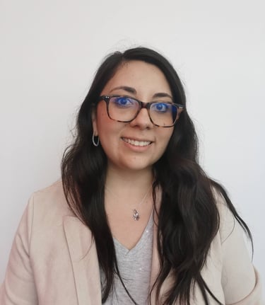 Smiling woman with long dark hair wearing glasses and a beige blazer against a white background.