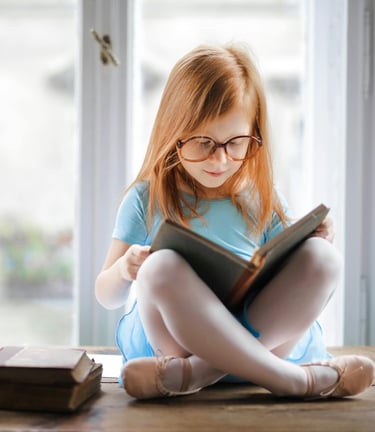 a young girl is sitting on a table with a book