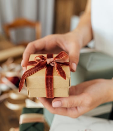 a person holding a small gift box with a red ribbon