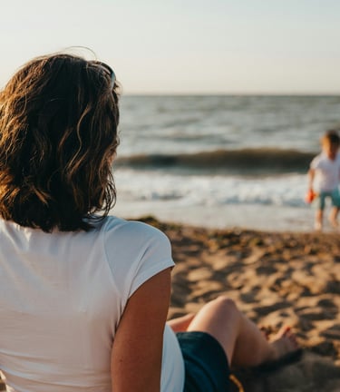 Mère assise sur la plage, face à la mer, regarde son fils jouer au bord de l'eau