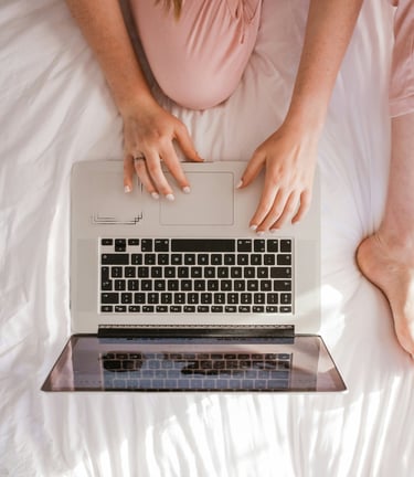 a woman sitting on a bed with her laptop computer