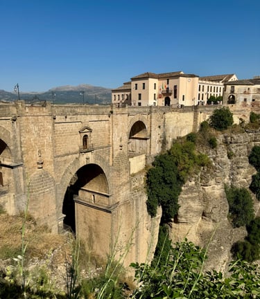 The historic Puente Nuevo stone bridge spans the El Tajo gorge in Ronda, Spain, under a clear blue sky.