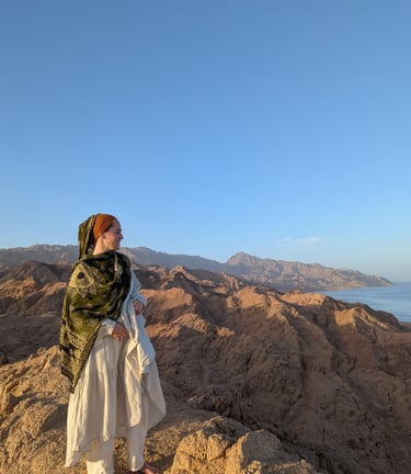 Woman standing on top a mountain with ocean in the background