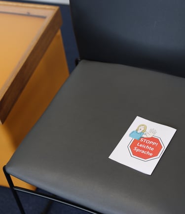 Die Sitzfläche eines Stuhls auf dem ein "Stopp - Leichte Sprache" Zettel liegt.