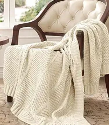Cream cable knit throw blanket draped over a vintage tufted armchair.