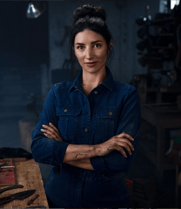 Editorial portrait of a female artisanal knifemaker: her arms are folded and she is staring straight at the camera.