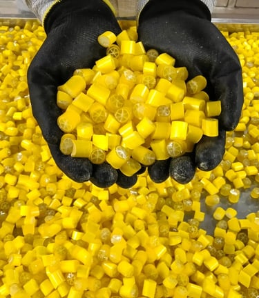 Gloved hands holding a pile of yellow lemon hard candies with a citrus cross-section design.