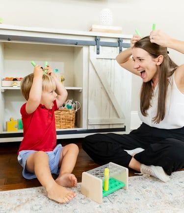 A therapist and child playing together, imitating each other making horns with a set of blocks 