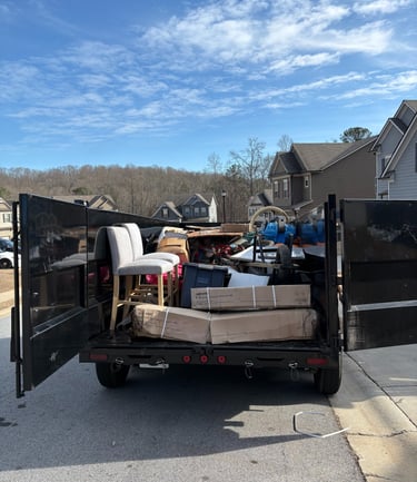 A black junk removal trailer filled with furniture, boxes, and debris for residential waste disposal.