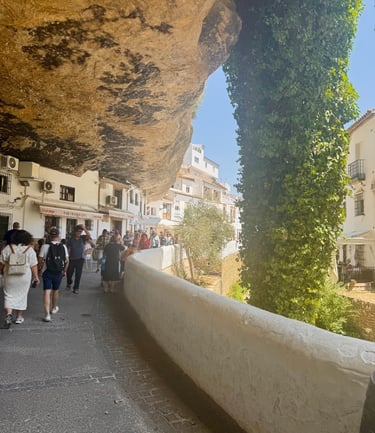 Tourists walk through Setenil de las Bodegas, a Spanish town with white houses built into cliffs.