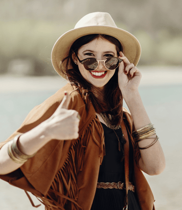 a woman in a hat and sunglasses is smiling and holding a cell phone