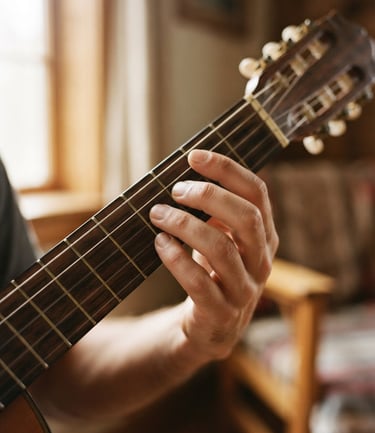 Intimate close-up of hands positioning on nylon guitar strings, warm natural light from a side window, rich wood textures of the classical guitar neck, shallow depth of field, 35mm film look.