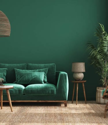 Sofá verde frente a una pared verde con mesa pequeña y flores empresa limpieza Marbella.
