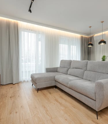 Nowoczesny salon z jasną narożną sofą, telewizorem, drewnianą podłogą i zasłonami.