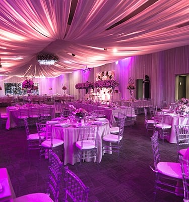 Salón de eventos elegante con pista iluminada, mesas decoradas y luces colgantes.