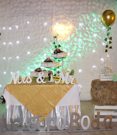 Mesa de boda decorada con pastel de varios niveles, luces y detalles dorados.