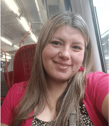 Una mujer sonriente con mechas rubias está sentada en un tren de cercanías con un cárdigan rosa.