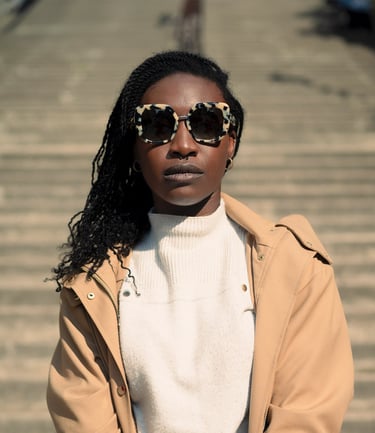 Portrait d’une modèle en manteau beige et lunettes léopard, posant sur des marches en plein soleil, regard confiant face à l’
