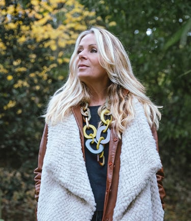 Portrait d’une modèle en extérieur, regardant sur le côté, portant un manteau clair et un collier imposant, avec un fond de f