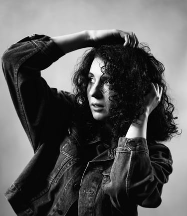 Portrait en noir et blanc d’une modèle aux cheveux bouclés, posant avec les bras levés dans une lumière contrastée.