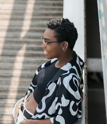 Portrait d’une modèle souriante en tenue noire et blanche, posant de profil contre une rambarde, avec un escalier en arrière-