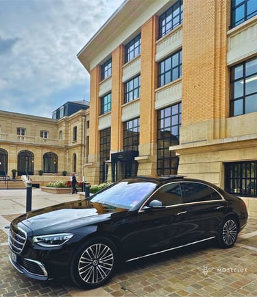 Black Mercedes-Benz S-Class luxury sedan parked in front of a modern European stone building.