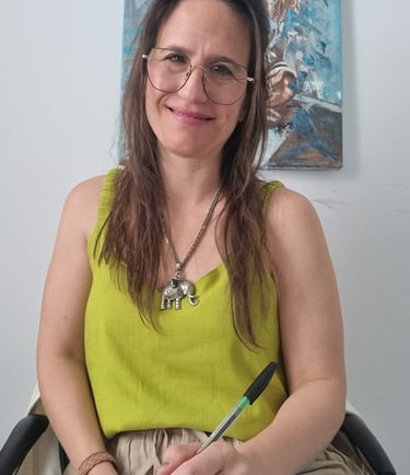 A smiling professional woman with glasses and an elephant necklace holding a pen and notepad.