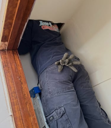 Professional HVAC technician on a ladder inspecting home ceiling ductwork and insulation.