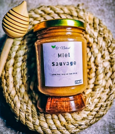 A glass jar of Miel Sauvage raw wild honey with a wooden dipper on a woven coaster.