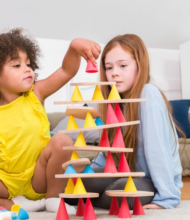 Two children creating a structure from colorful silicone cones and wooden tables in the room