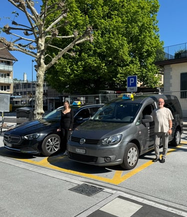 Zwei Taxiautos. Ein grauer VW Caddy und ein schwarzer Mercedes E-Klasse samt Taxifahrer