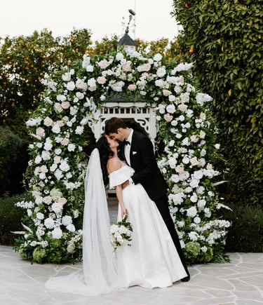 a bride and groom kissing in front of a floral arch