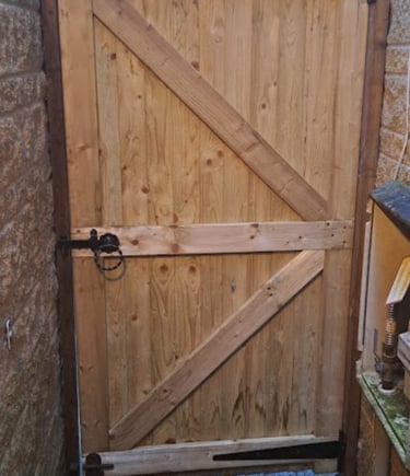 Close-up of a sturdy braced wooden side gate with black iron hinges and latch installed between two stone walls.
