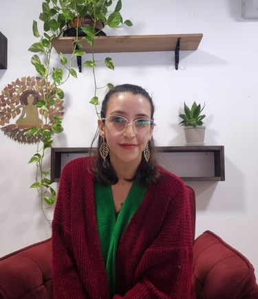 Mulher de óculos e brincos olhando para a câmera sorrindo com plantas e buda ao fundo