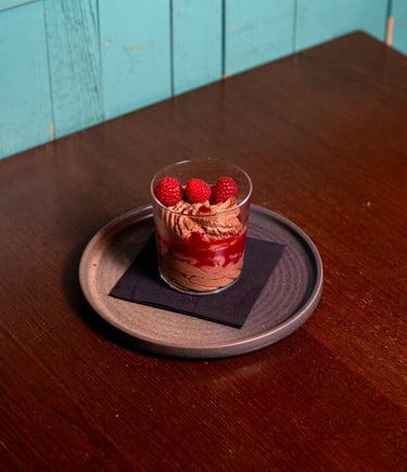 Schokolmbeer-Faden-Soufflé im Glas mit Hiruchtpüree und frischen Himbeeren, serviert auf einem runde